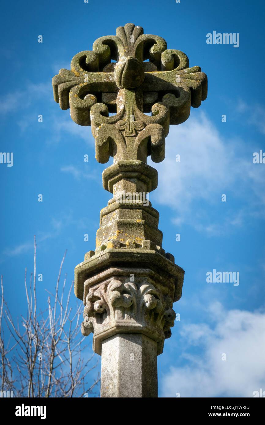 Piedra ornamentada tallada cruz sobre una estrecha columna de piedra contra un cielo azul Foto de stock