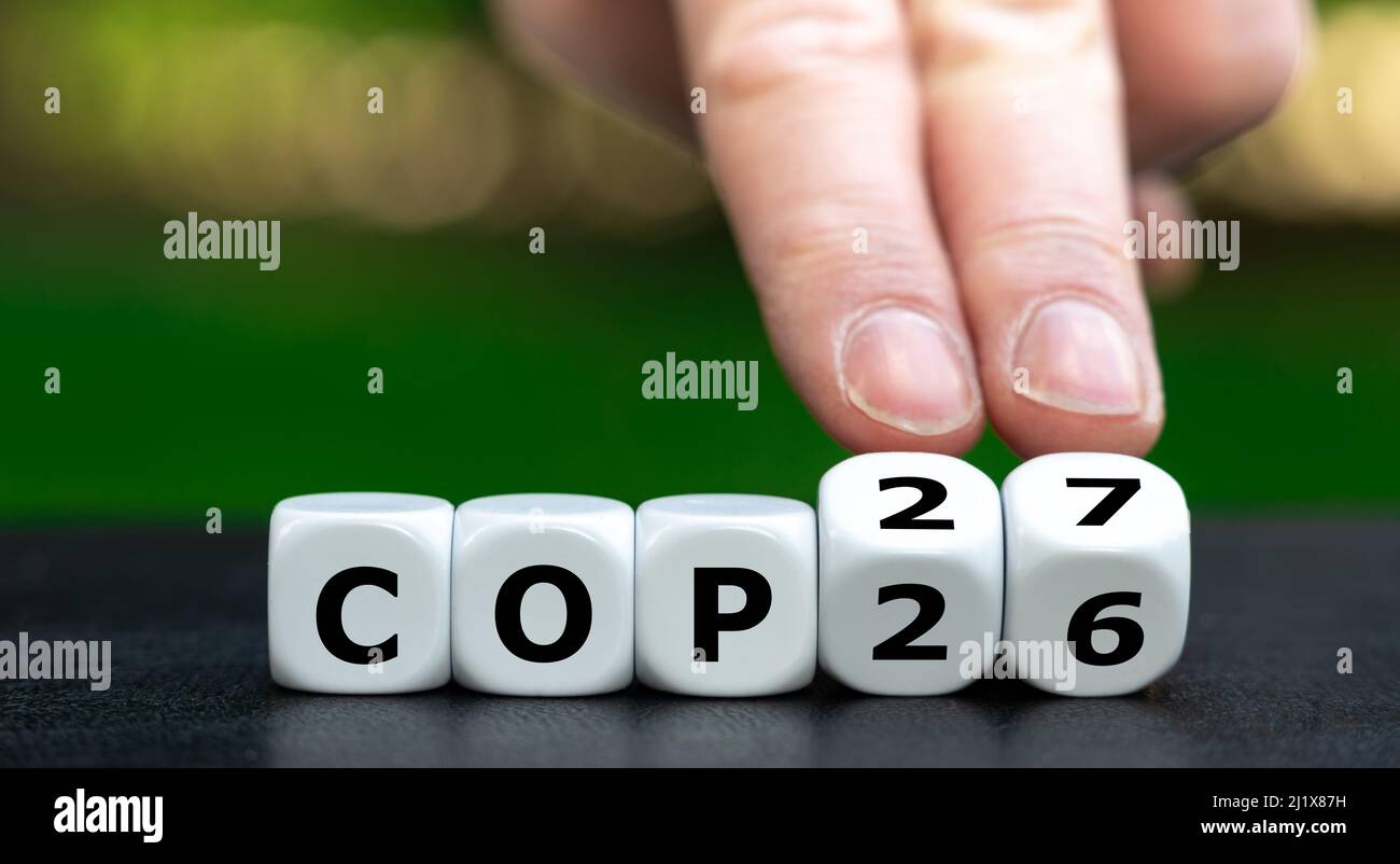 Símbolo de la próxima conferencia sobre el cambio climático COP27. La mano da vuelta a los dados y cambia la expresión COP26 a COP27. Foto de stock