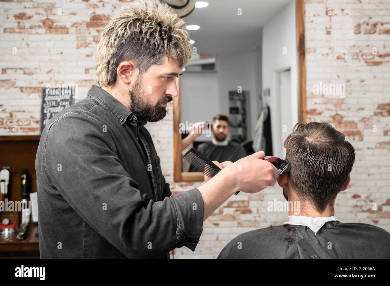 Hombre barbero cortando pelo de cliente masculino con cortapelos