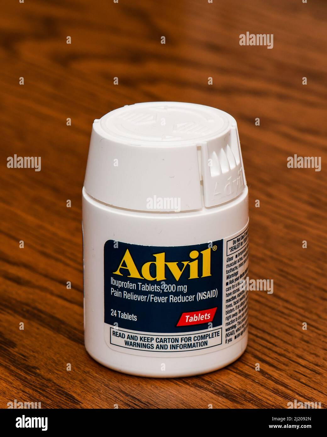 Una botella de plástico blanca de 24 comprimidos recubiertos de Advil, 200 mg de Ibuprofeno, un analgésico y un reductor de fiebre AINE aislados en un escritorio de roble Foto de stock