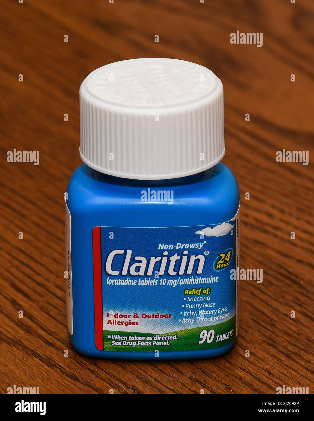 Una botella azul de 90 comprimidos de Claritin, loratadina Un antihistamínico no ahogado para el alivio de la alergia en interiores y exteriores aislado en un escritorio de roble. Foto de stock