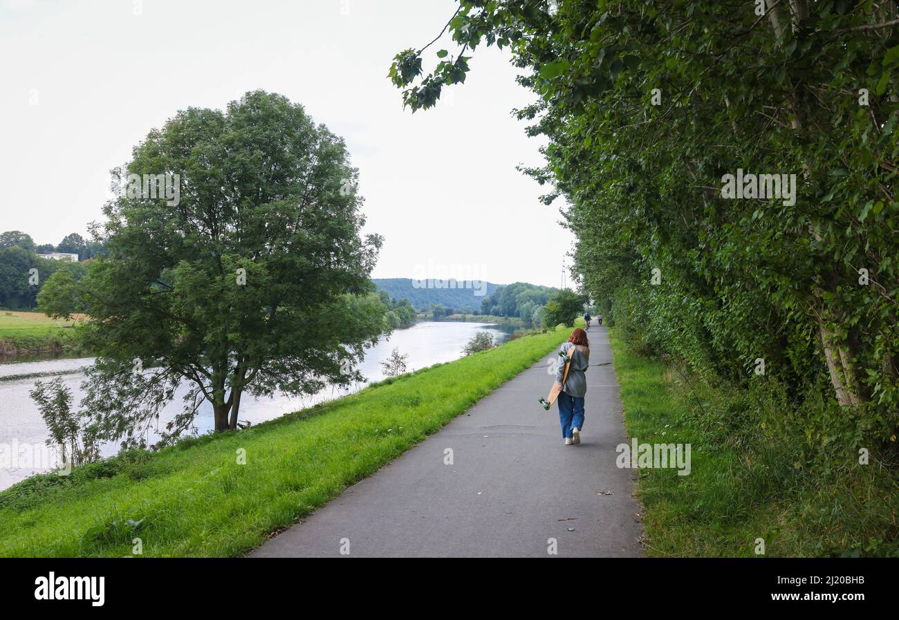 04.08.2021, Alemania, Renania del Norte-Westfalia, Hattingen - Paisaje en el Ruhr, Ruhrpromenade, mujer joven con skateboard en el camino al skate Foto de stock