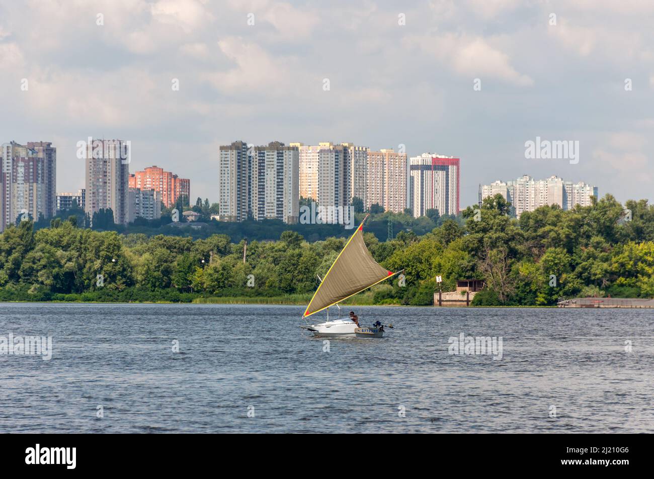 Kiev, Ucrania - 3 de julio de 2021: un velero y un pequeño barco Kiddy están navegando a lo largo del río Dnipro en el fondo de una zona residencial en Kiev, Foto de stock