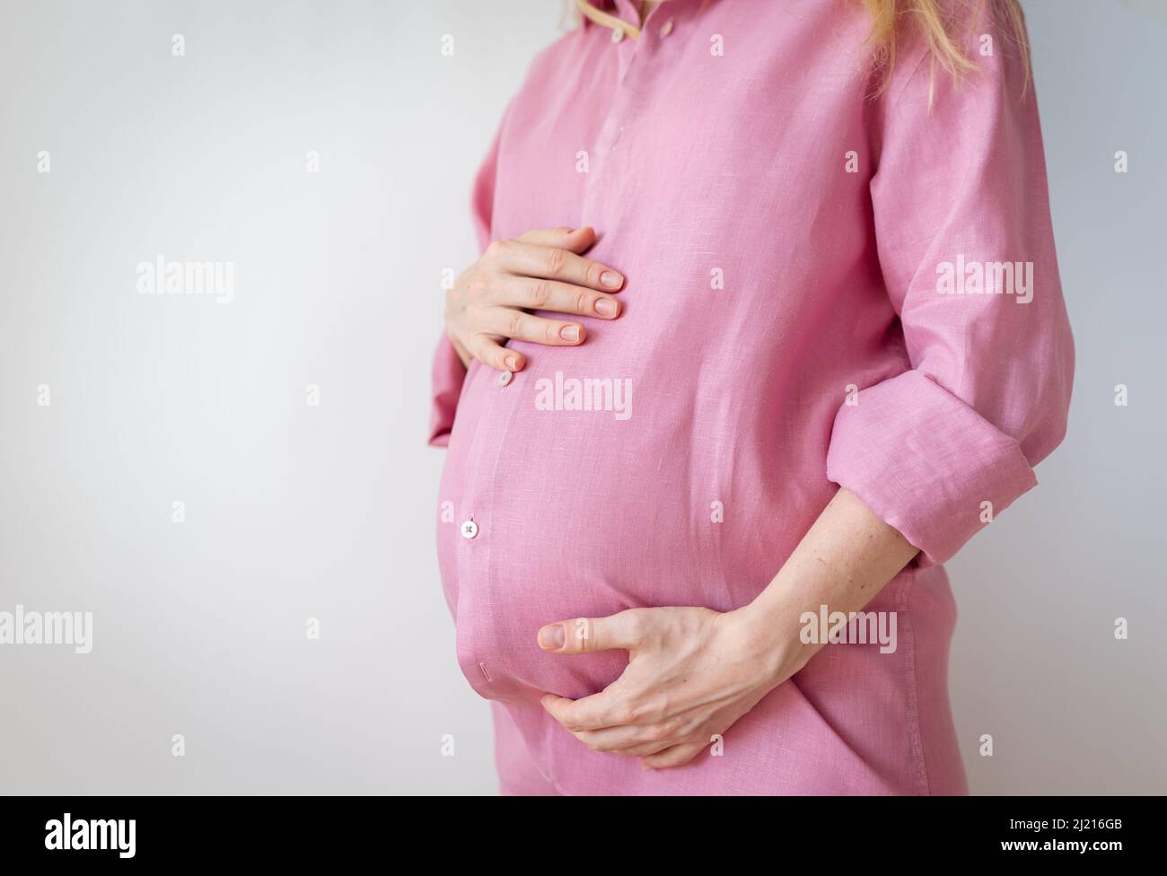 una mujer embarazada está de pie con las manos en su estómago, el concepto de esperar un bebé Foto de stock
