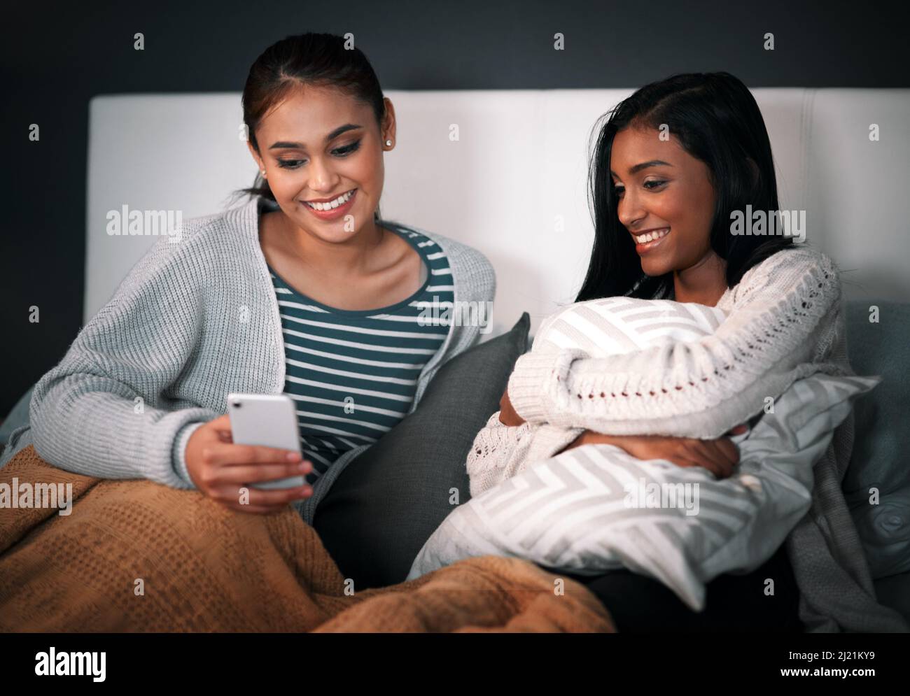 Disfrutar de algunos acecho en línea. Foto de una mujer joven mostrando a su amiga algo en su teléfono móvil mientras se sienta juntos en una cama. Foto de stock