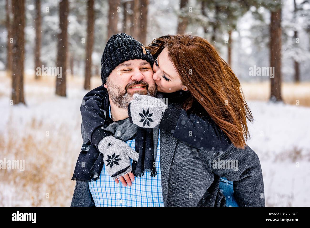 Mujer besando al hombre desde atrás en un bosque de pino nevado Foto de stock