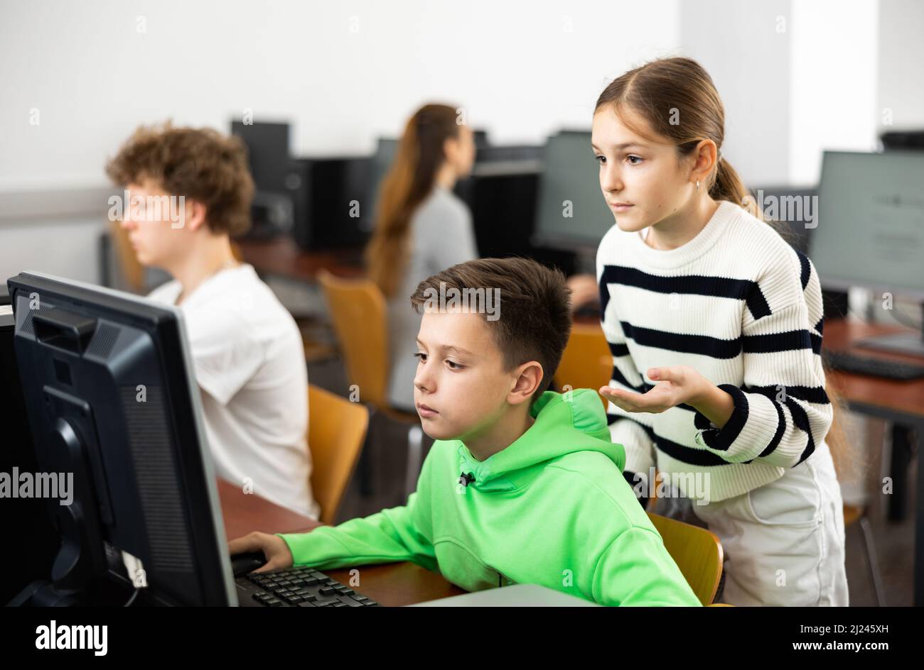 Una niña adolescente ayudando a un compañero de clase enfocado sentado en la computadora en clase Foto de stock