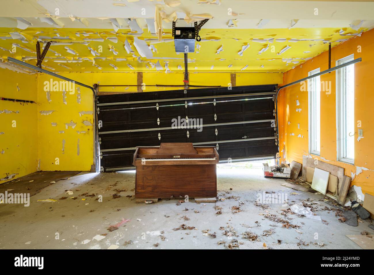 Un piano sentado en un garaje amarillo brillante con una puerta rota. Esta casa ha sido demolida desde entonces. Foto de stock