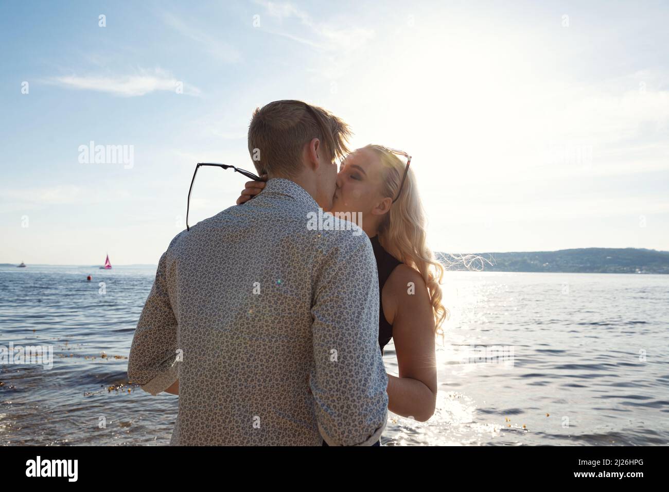Pareja besándose en la playa contra el sol Foto de stock