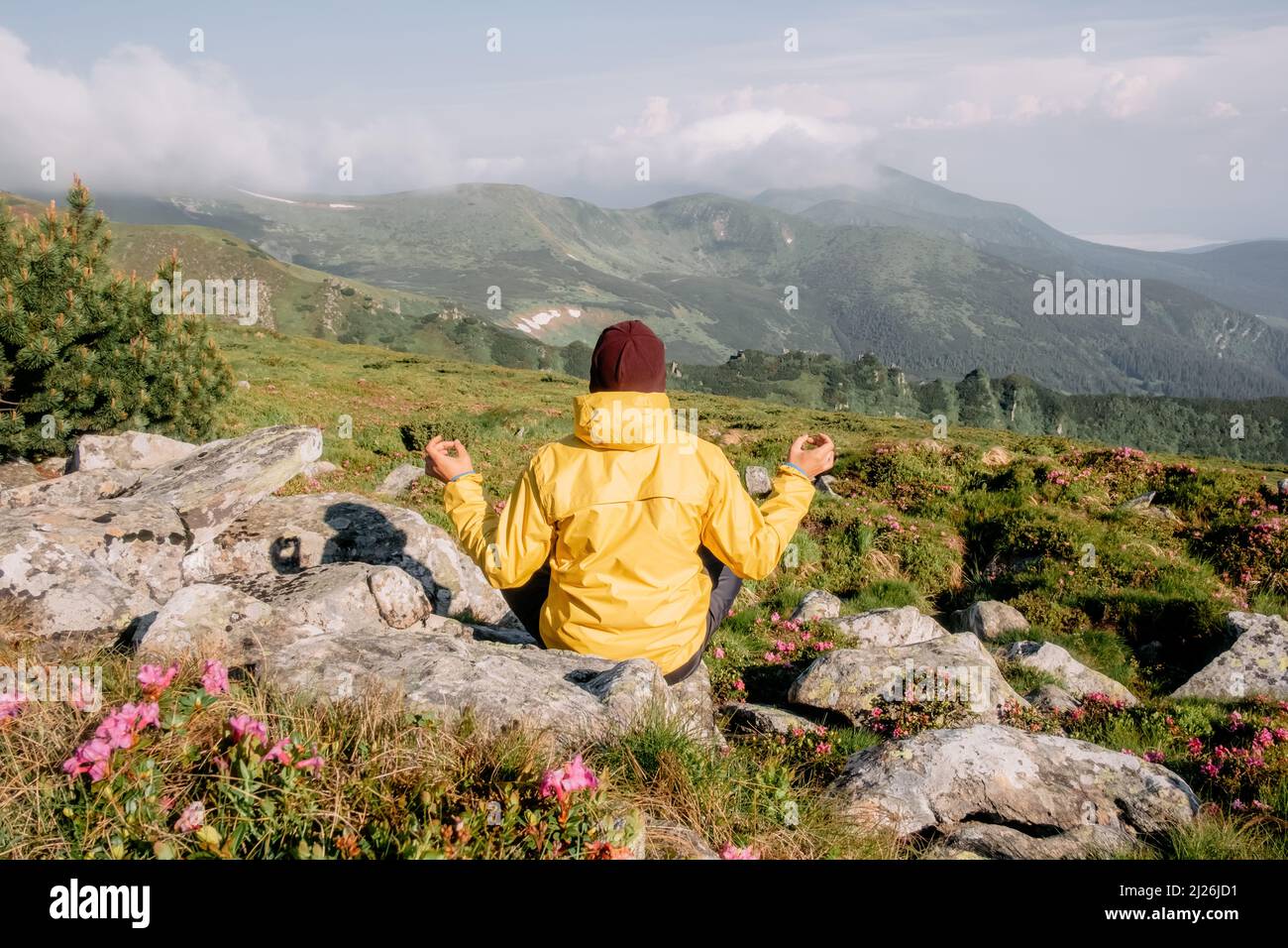 Solo turista en chaqueta amarilla medita en altas montañas Foto de stock
