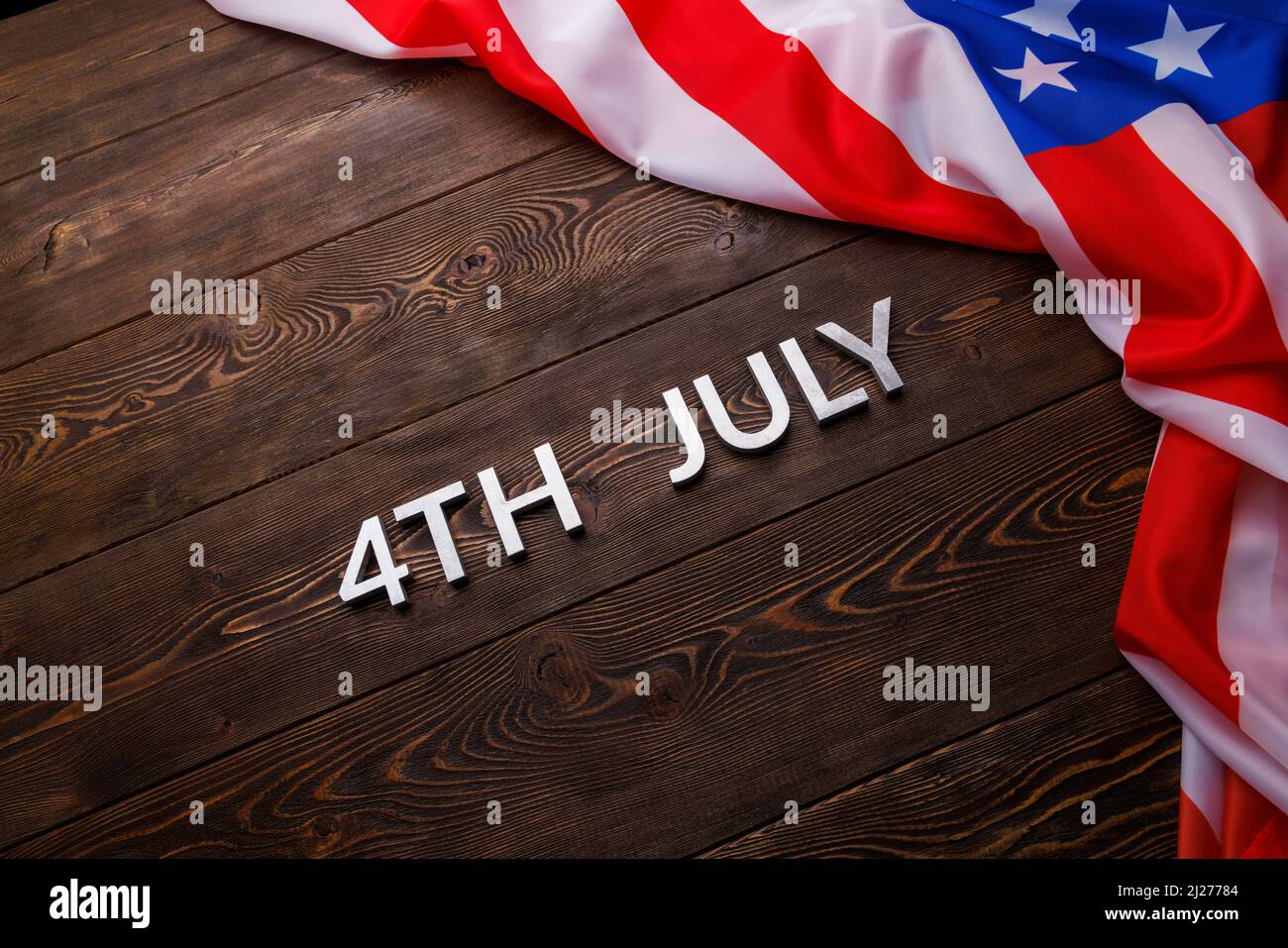 las palabras 4th de julio y la bandera de ee.uu. arrugada sobre fondo de superficie de madera de textura plana. Foto de stock