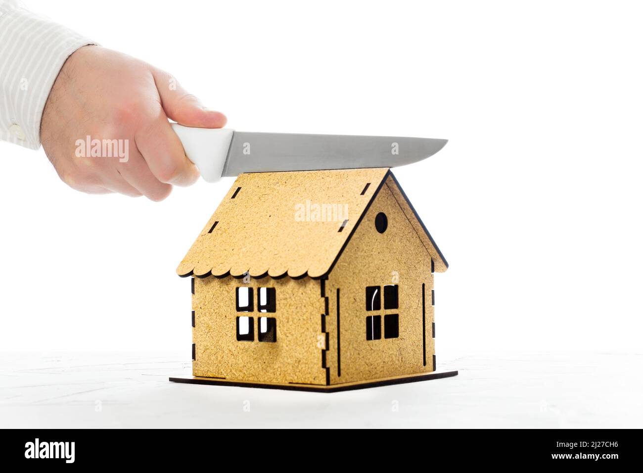 Macho cortando a mano un modelo de casa en miniatura con un cuchillo de cocina por la mitad. La división del hogar en un divorcio. Foto de stock
