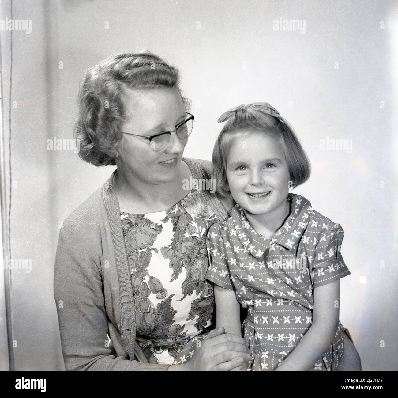 1961, histórica, foto de estudio de la era, una joven dulce con un arco en su pelo, sentada con su madre para su foto, Stockport, Manchester, Inglaterra, Reino Unido. Foto de stock