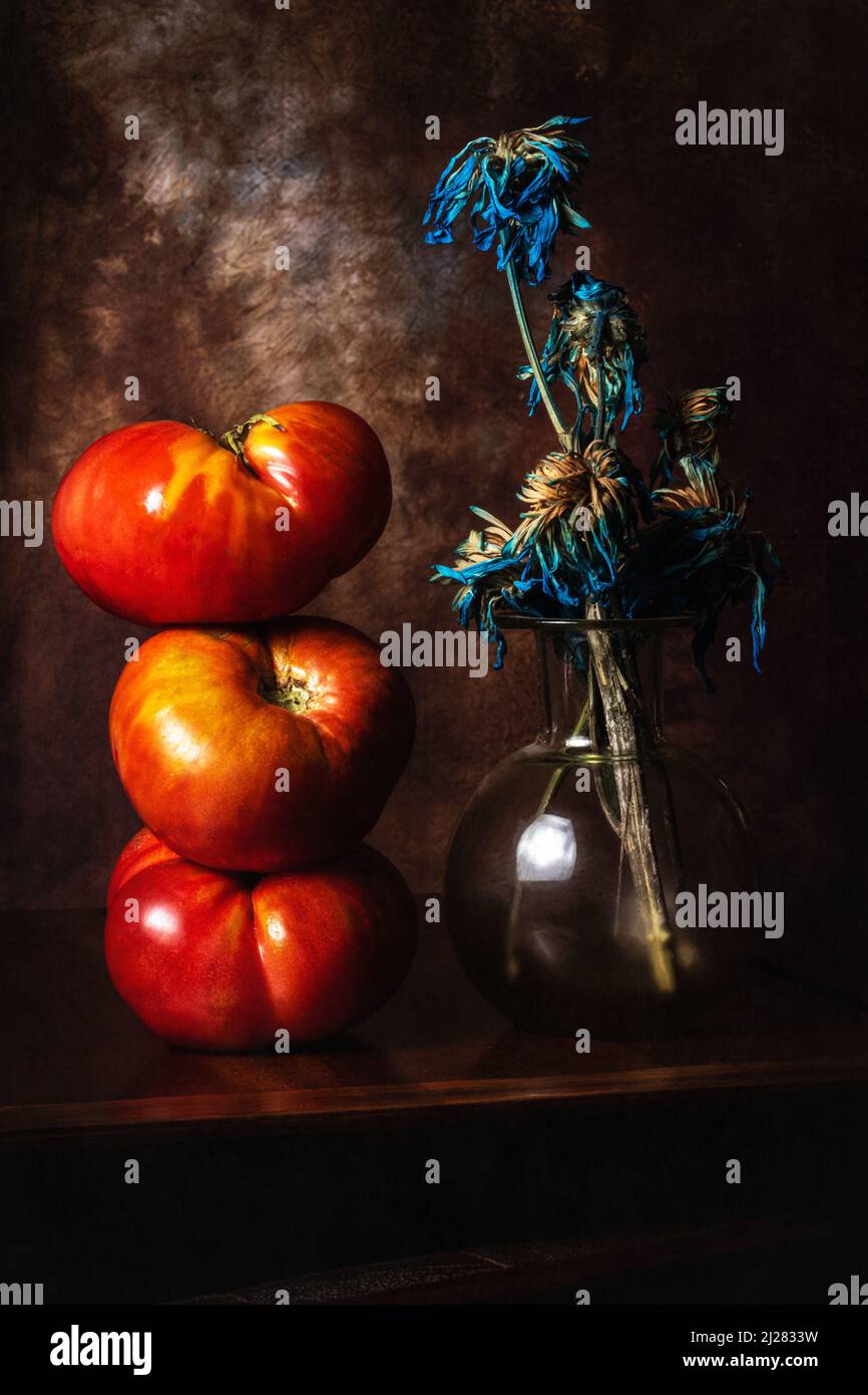 Vida de quieto temática, simetría de tomates y flores secas azules. / Foto de stock