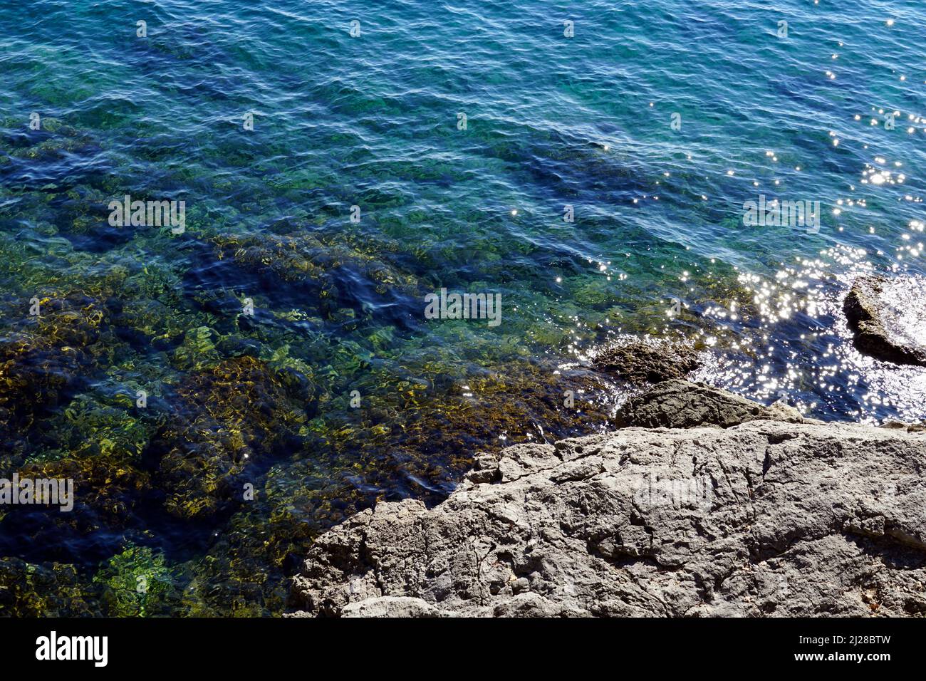 Agua de mar espumosa y ecológicamente clara a lo largo de la costa rocosa en un hermoso día soleado Foto de stock