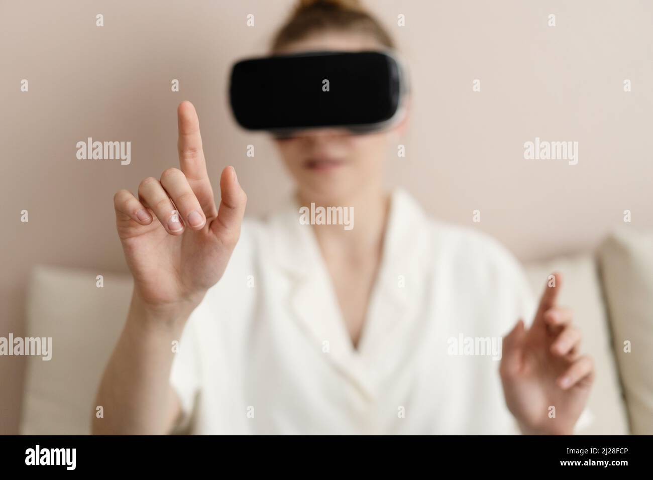 Disfrutar de la nueva realidad. Atractiva mujer joven con auricular VR que gestora y sonríe mientras está sentada en casa Foto de stock