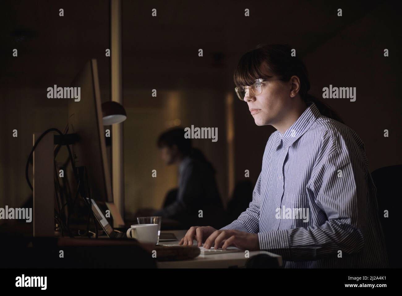Joven empresaria que utiliza la computadora mientras trabaja tarde en la oficina por la noche Foto de stock