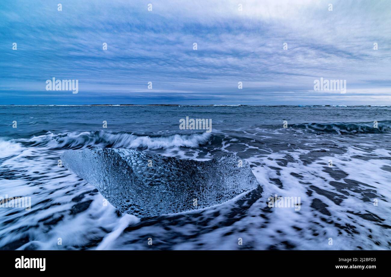 Pequeños bloques de hielo y olas entrantes en Diamond Beach con arena negra, Breidamerkursandur, Islandia Foto de stock