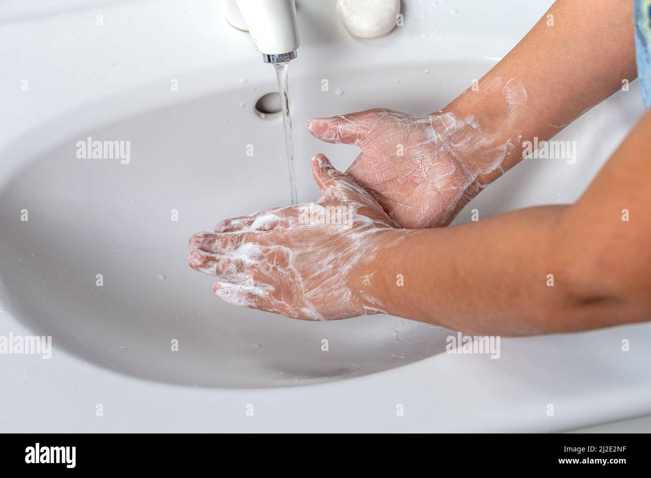 Mujer lavando la mano con espuma de jabón y agua del grifo en el baño. Limpiar a mano bajo el grifo del fregadero para la higiene personal para prevenir la gripe y el coronavirus. Buen procedimiento de lavado de manos para matar bacterias, virus Foto de stock