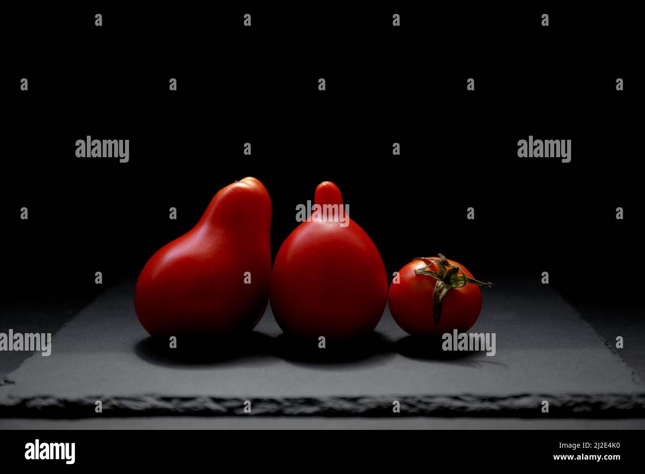 Tres tomates rojos sobre fondo negro. Tomate aislado, vista lateral. Antioxidantes naturales en tomates Foto de stock