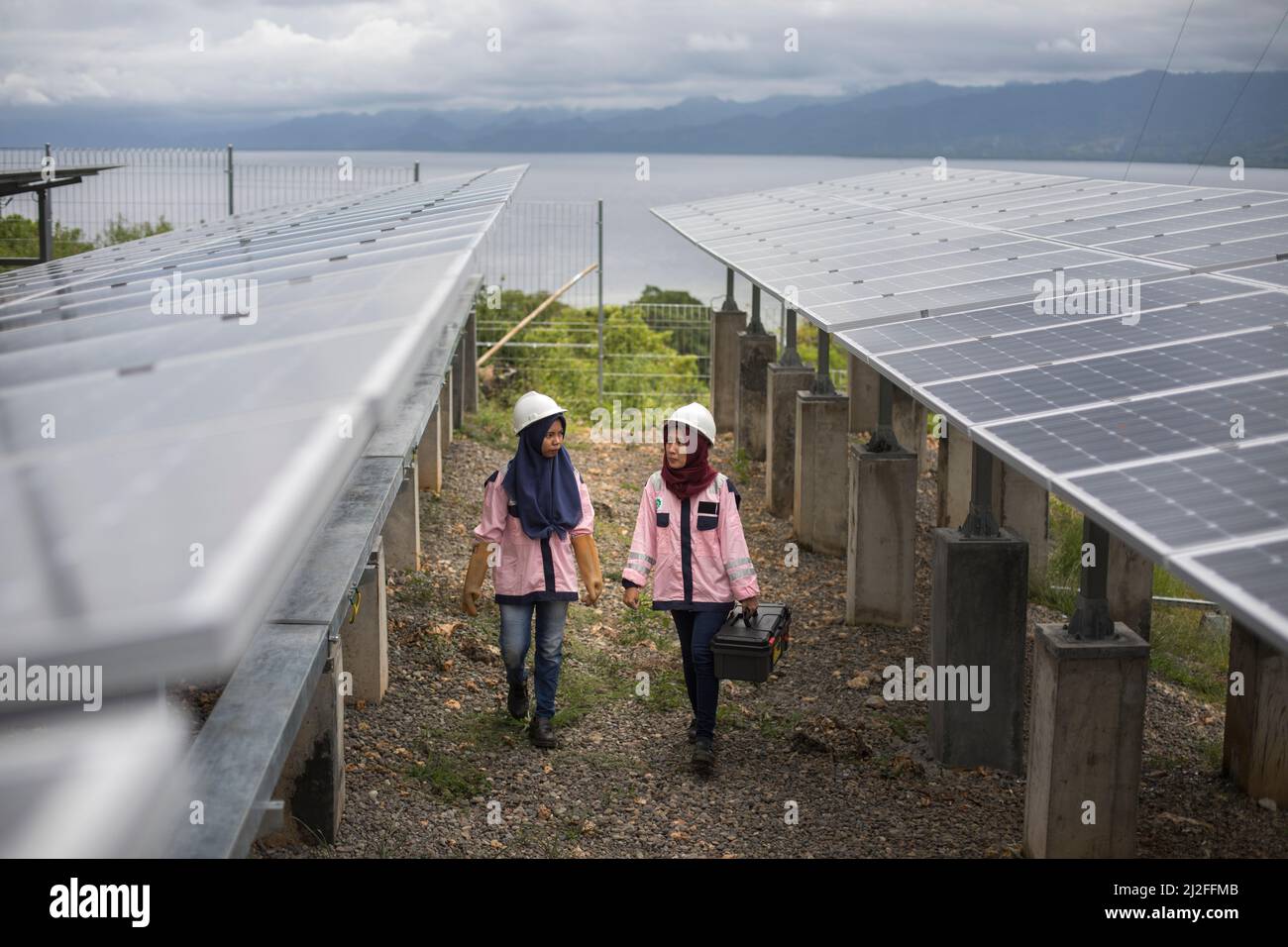 Los técnicos eléctricos subalternos de Karmila (23, l) y Verawati (25, r) inspeccionan y mantienen paneles solares en la isla de Karampuang, Indonesia, que estaban inst Foto de stock