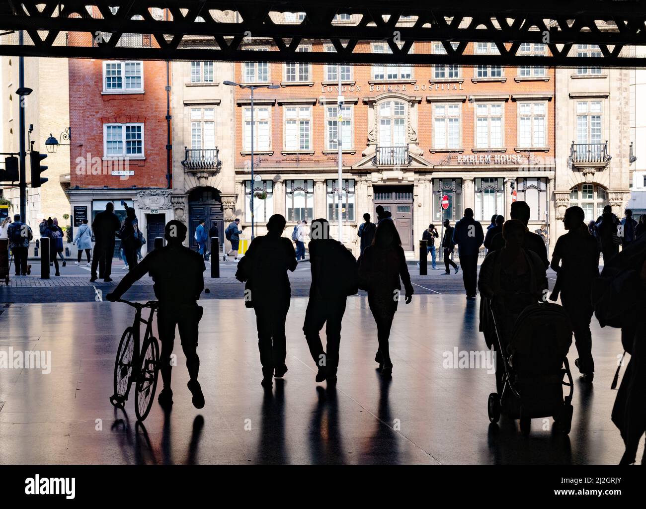 Silueta de gente normal; Grupo de personas caminando en la estación del Puente de Londres con bicicleta y cochecito emergiendo en la calle, Londres Reino Unido Foto de stock