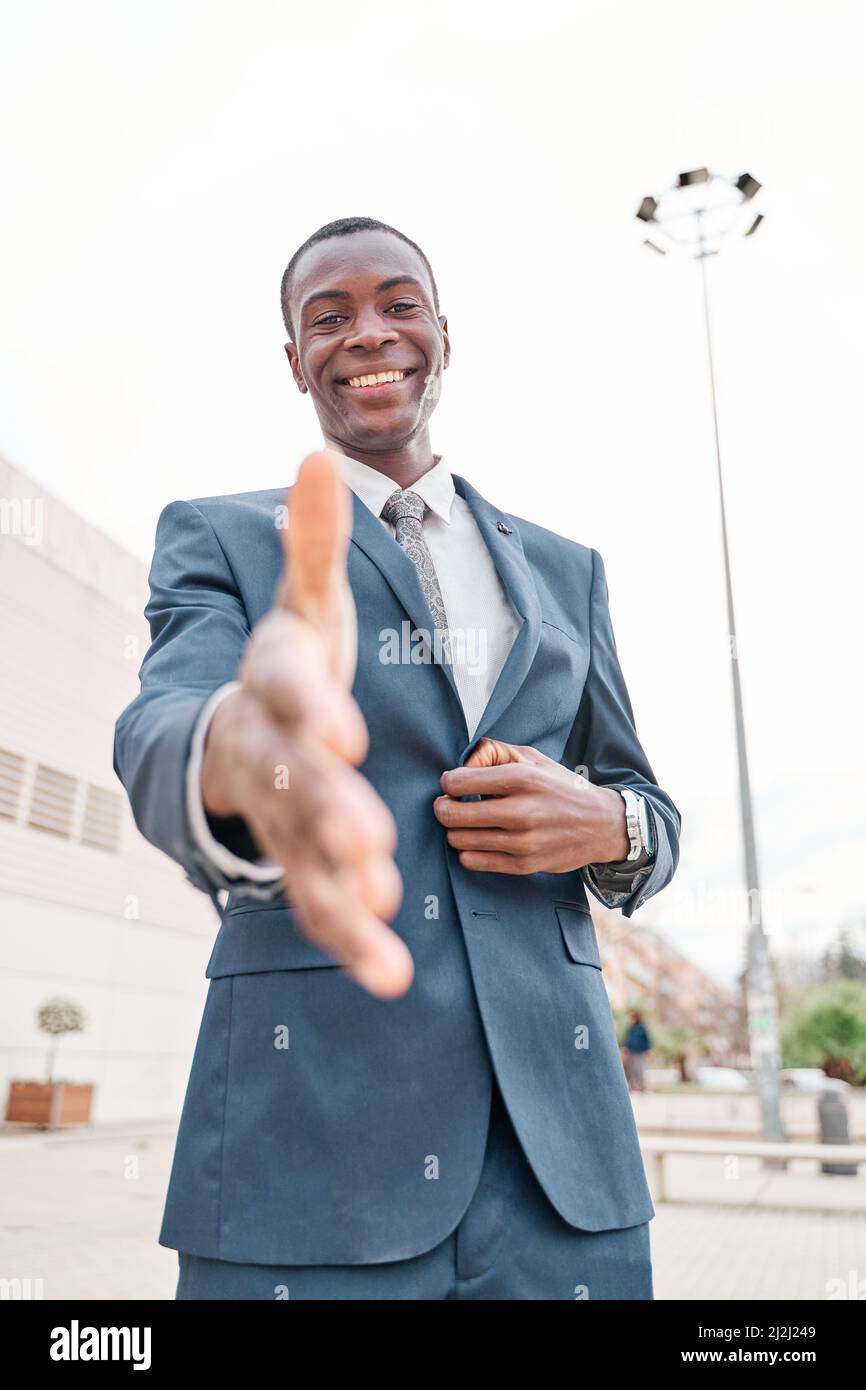 retrato de un joven hombre de negocios afroamericano sonriente mirando la cámara y extendiendo el brazo para el apretón de manos. Concepto de trato y acogedor Foto de stock