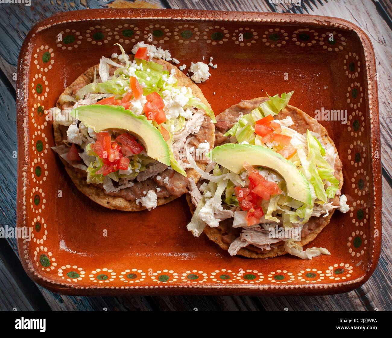 Tostadas de comida mexicana tradicional en un plato de barro o arcilla  sobre una mesa rusca con pollo o carnitas, lechuga, tomate, cebolla,  frijoles fritos, picante Fotografía de stock - Alamy