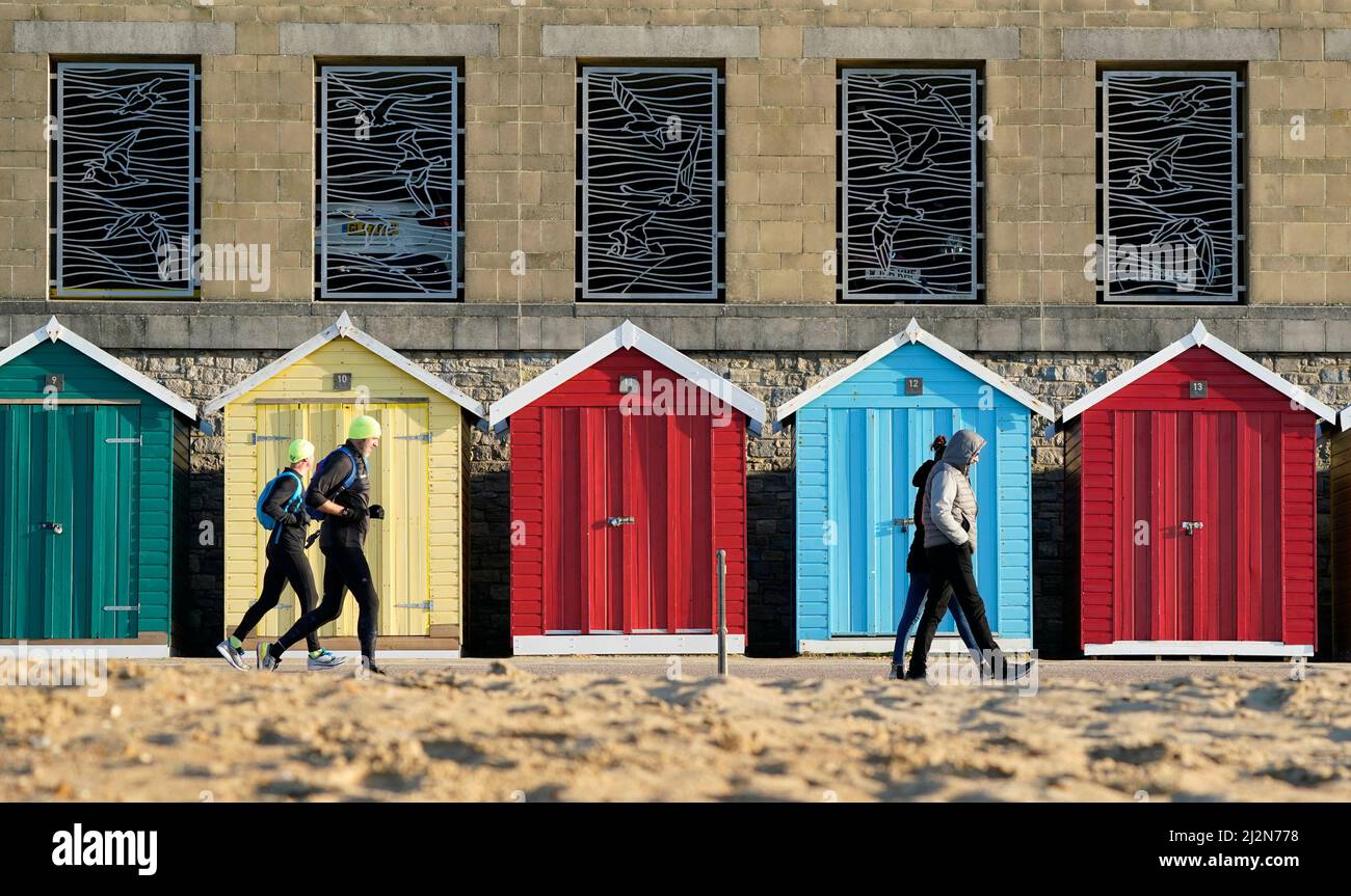 La gente pasa por cabañas de playa en la playa de Boscombe en Dorset. Fecha de la foto: Domingo 3 de abril de 2022. Foto de stock