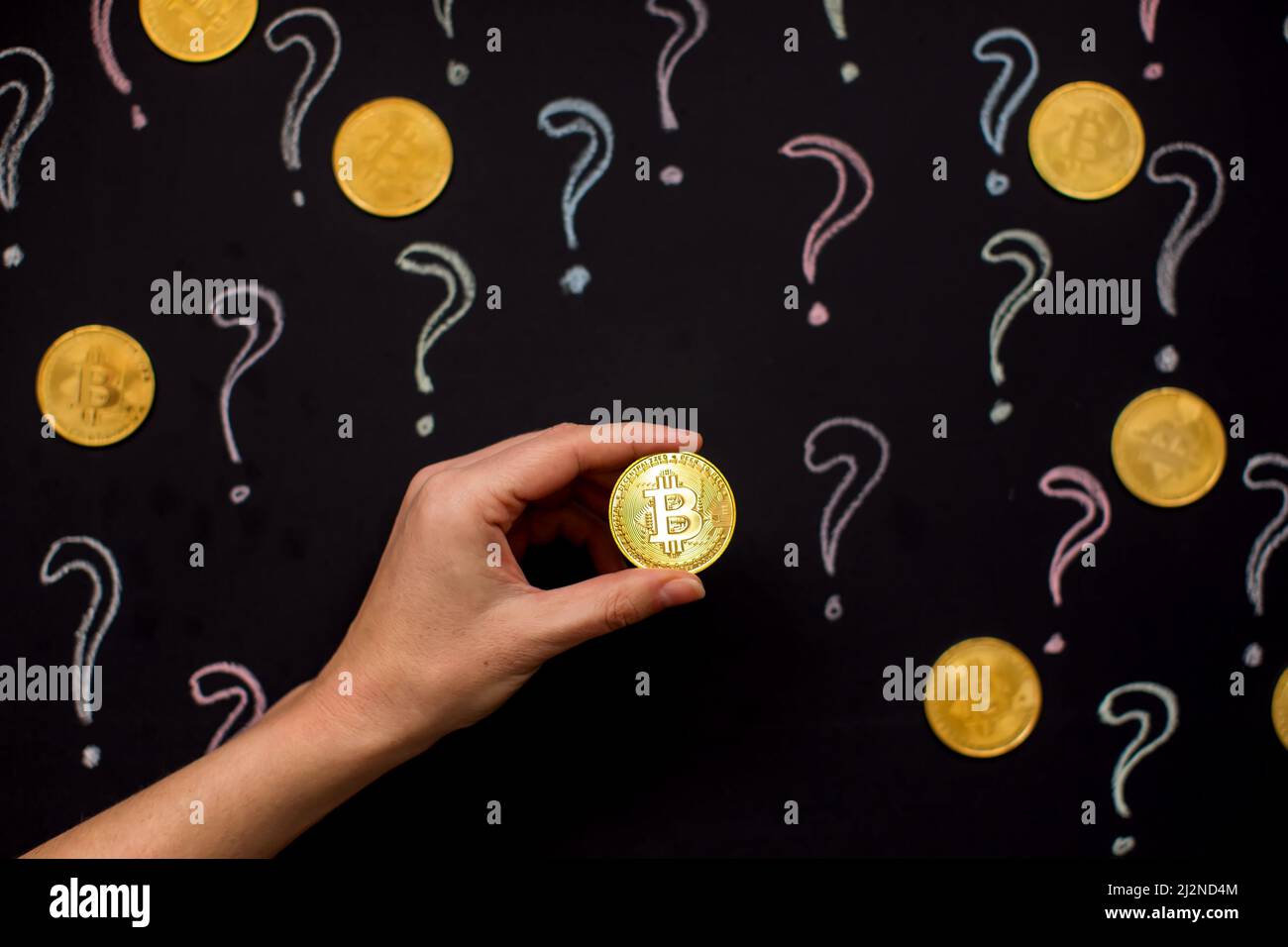 Mano sosteniendo Bitcoin dinero virtual contra pizarra con signos de interrogación. Concepto de moneda digital Foto de stock