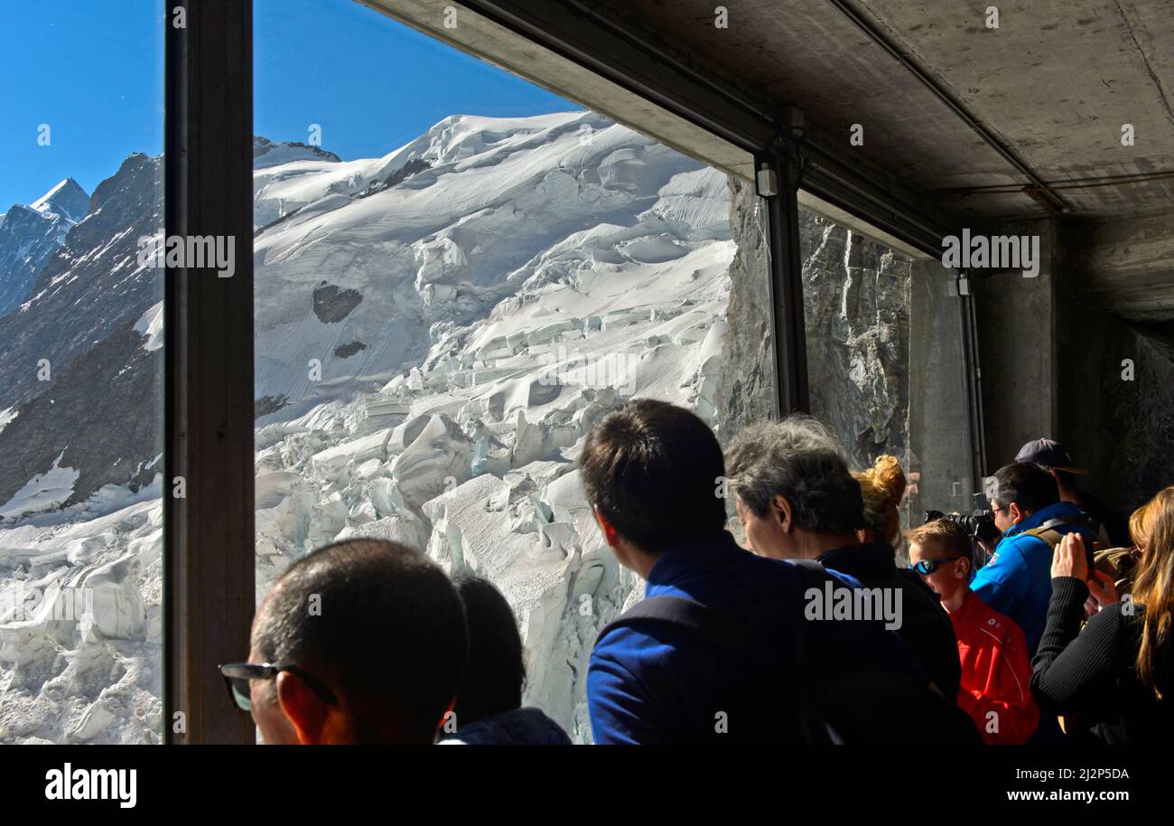 Los turistas miran a través de una ventana de cristal a las paredes de hielo del glaciar Eiger en la estación Eigerwand del ferrocarril Jungfrau, Grindelwald, Suiza Foto de stock