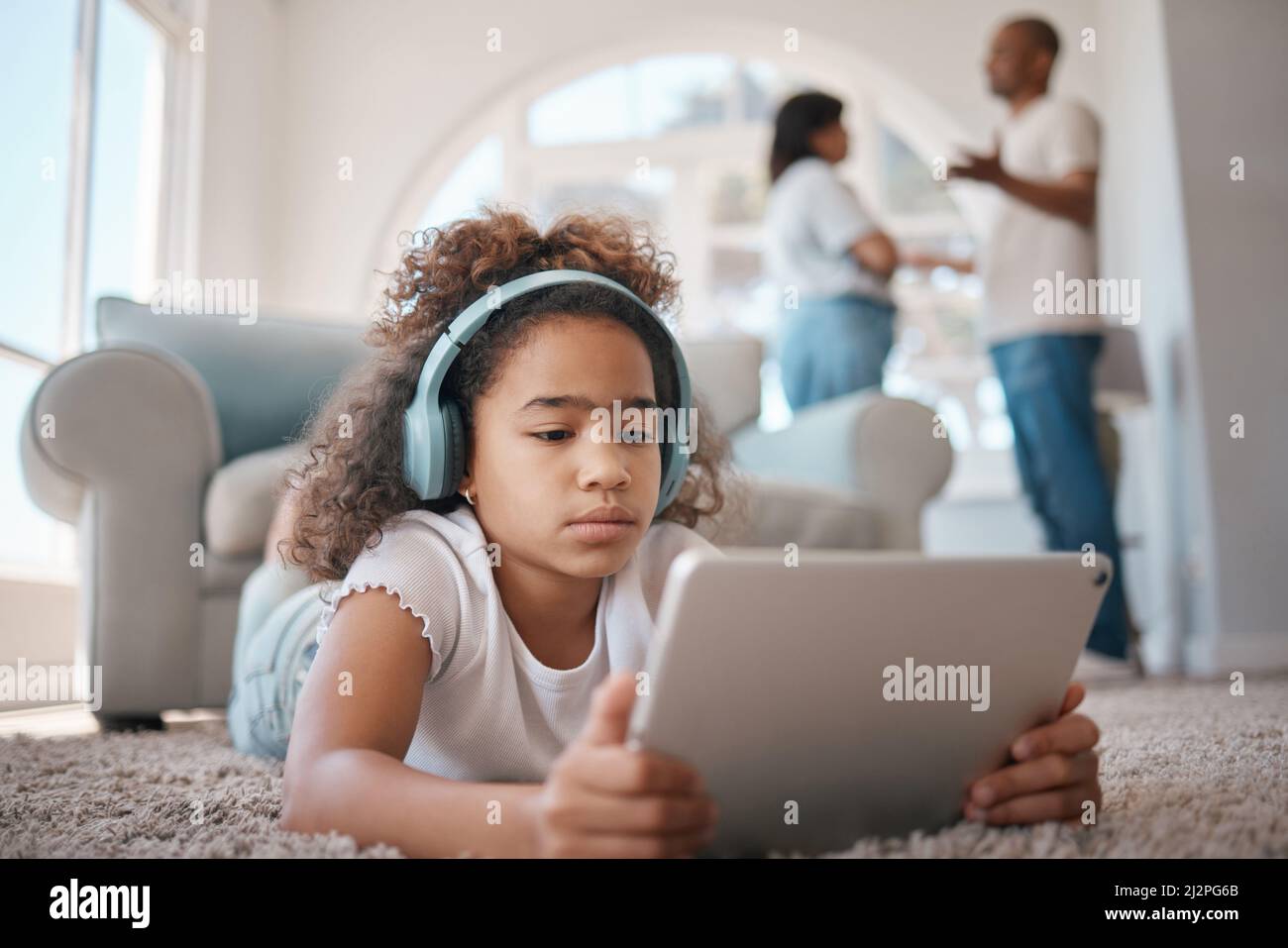 Las cosas se ven rocosas. Foto de una niña usando una tableta digital mientras sus padres argumentan. Foto de stock
