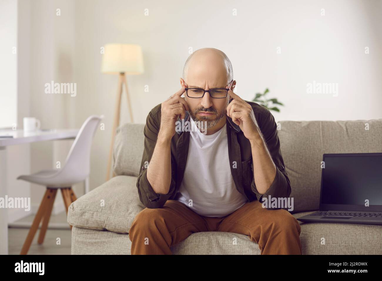 Un hombre serio y perplejo sentado en el sofá y pensando, tratando de responder a una pregunta difícil Foto de stock