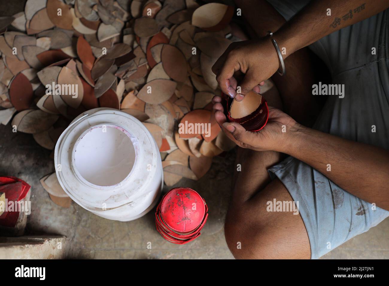 Un empleado aplica pegamento al cuero de una bola de cricket en una fábrica. La Indian Premier League (IPL), la competición de cricket más rica del mundo, es una liga profesional de cricket masculina de Twenty20, disputada por diez equipos de diez ciudades indias. Se jugará un total de 70 partidos de liga y 4 partidos de Playoff durante 65 días. La temporada 15th se iniciará el 26th de marzo de 2022. Foto de stock