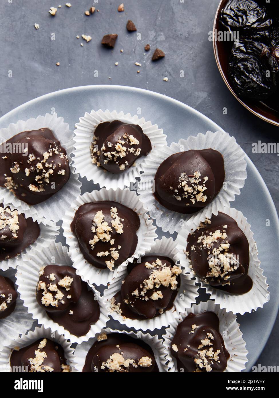 Dulces caseros de chocolate vegano crudo sin azúcar sanos con ciruelas secas y nueces sobre fondo azul plano Foto de stock