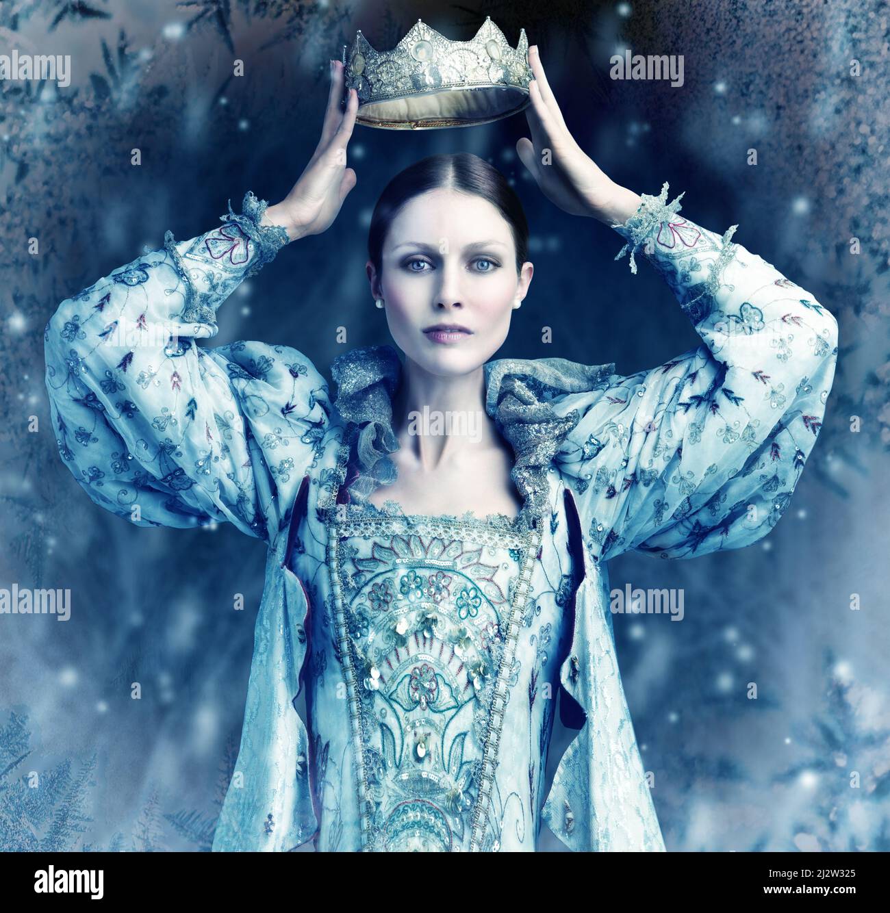La reina del hielo viene. Tiro de reina sosteniendo una corona sobre su cabeza con nieve cayendo alrededor de ella. Foto de stock
