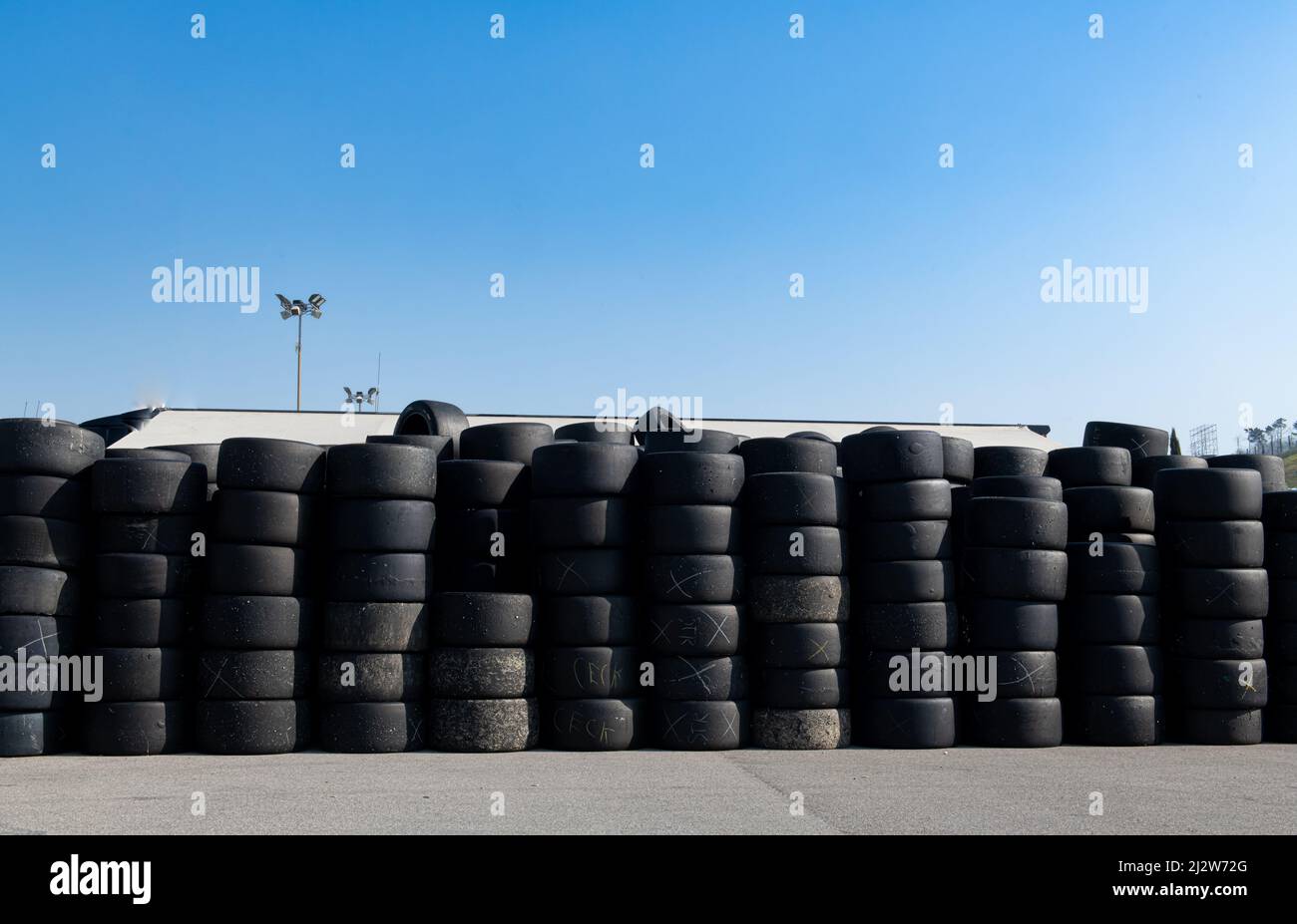 Gran grupo de viejos neumáticos de carreras usados apilados contra el cielo azul Foto de stock