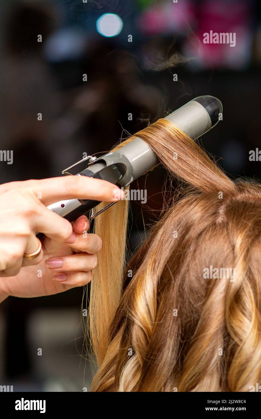 Peluquería hace rizos con una plancha para rizar para la mujer joven con el pelo largo en un salón de belleza Fotografía de stock - Alamy