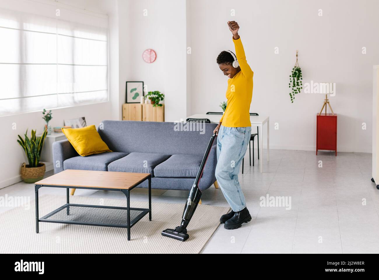 Feliz joven africana sofá de limpieza con un aspirador en casa Fotografía  de stock - Alamy