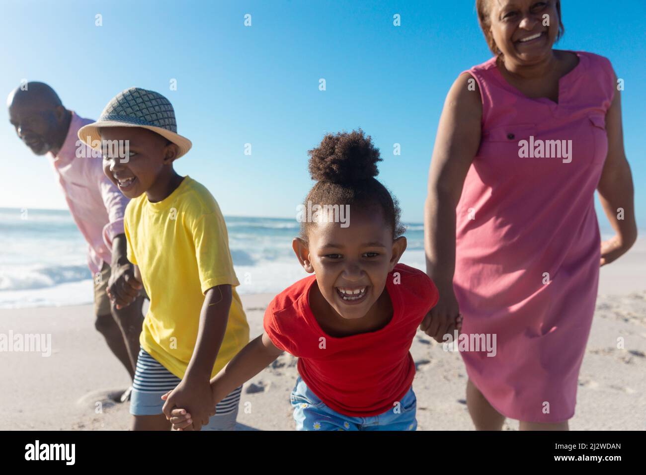 Felices nietos afro americanos que sostienen las manos mientras jalan a los abuelos en la playa Foto de stock