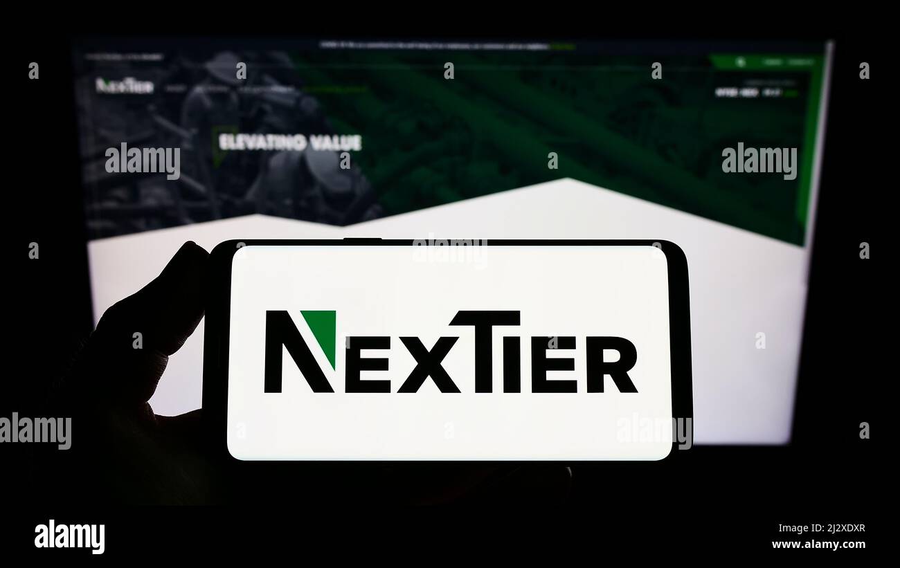 Persona que sostiene un smartphone con el logotipo de la compañía estadounidense NexTier Oilfield Solutions Inc. En la pantalla frente al sitio web. Enfoque en la pantalla del teléfono. Foto de stock