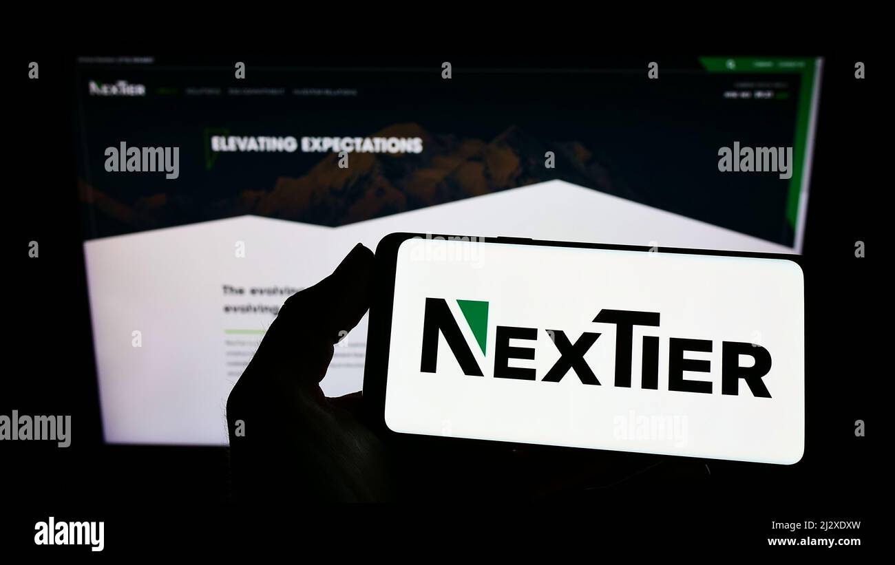 Persona que sostiene el teléfono móvil con el logotipo de la compañía estadounidense NexTier Oilfield Solutions Inc. En la pantalla frente a la página web. Enfoque en la pantalla del teléfono. Foto de stock