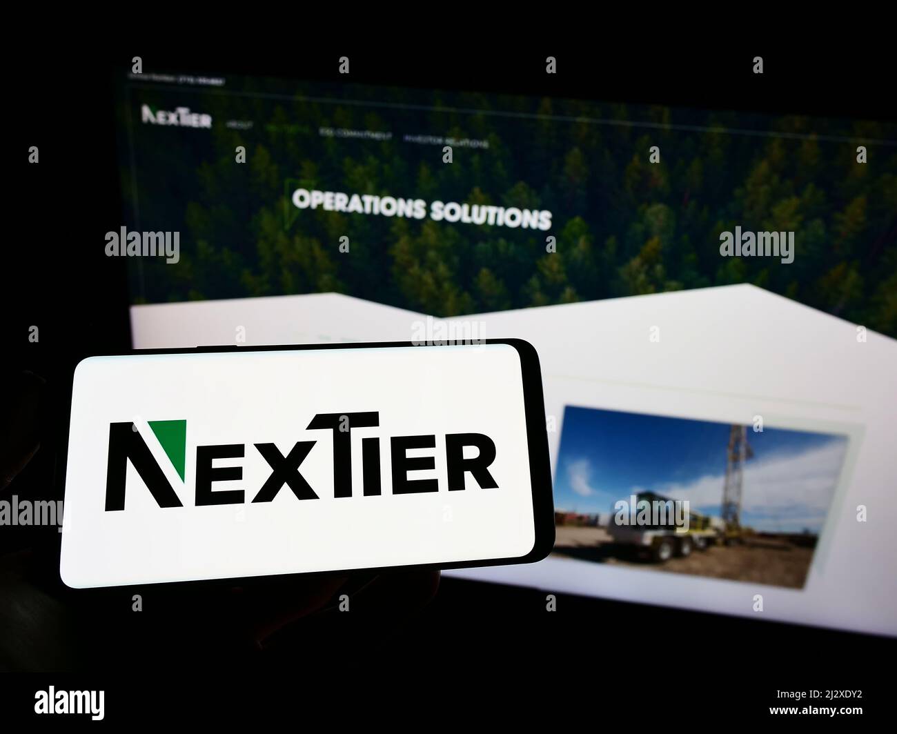 Persona que sostiene el teléfono móvil con el logotipo de la compañía americana NexTier Oilfield Solutions Inc. En la pantalla delante de la página web. Enfoque en la pantalla del teléfono. Foto de stock
