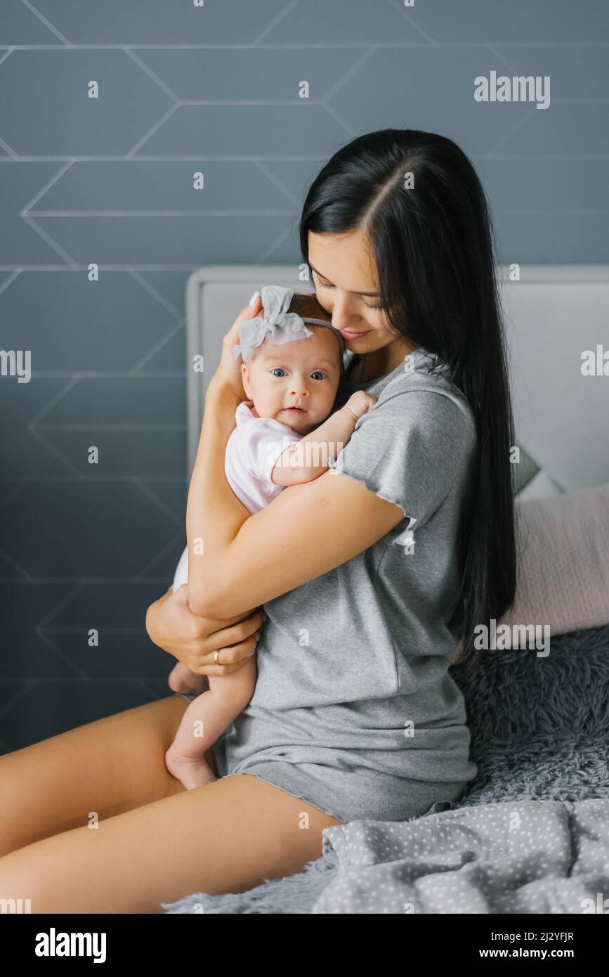 Hermosa joven madre sostiene a su hija en sus brazos, la mira y le sonríe Foto de stock