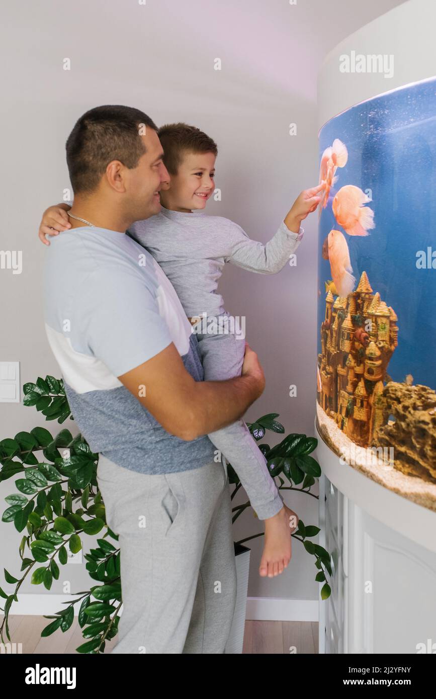 Papá y su hijo pequeño en sus brazos miran el acuario en su casa Foto de stock