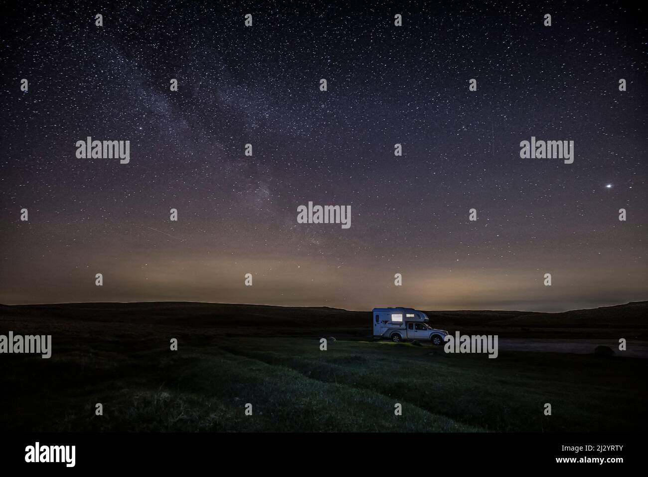 Camioneta autoiluminada, camioneta autocaravana por la noche bajo cielo estrellado, forma lechosa. Foto de stock