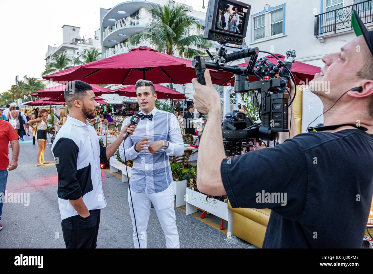 Miami Beach Florida, Ocean Drive, Nochevieja, reportero hombre negro sosteniendo el micrófono entrevistando al camarógrafo camarógrafo, REVUELTA TV social media Foto de stock