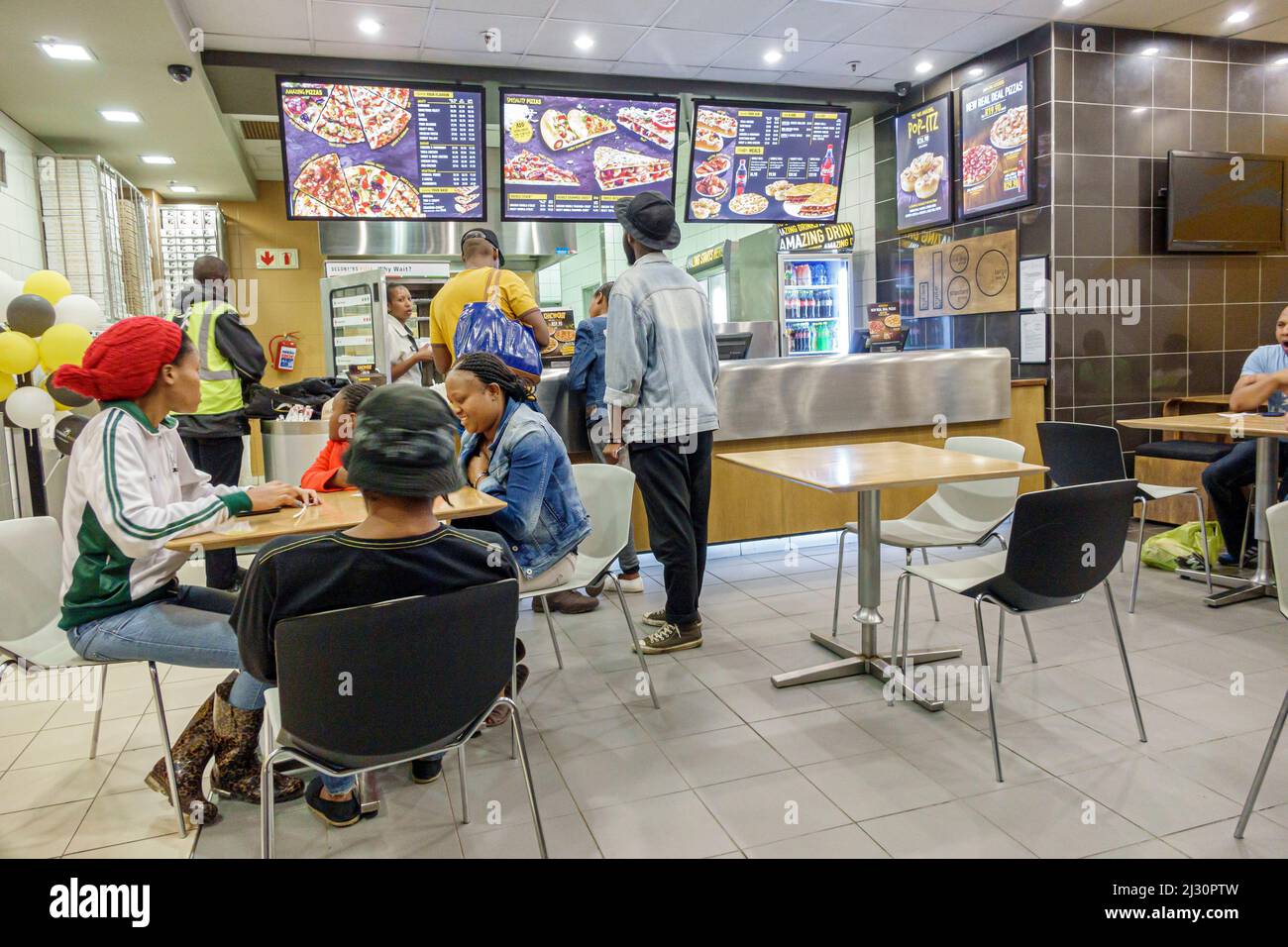 Johannesburgo Sudáfrica, African Rosebank, The Zone Mall, Debonairs Pizza, restaurante, interior mesas clientes, Black men menú para mujeres Foto de stock