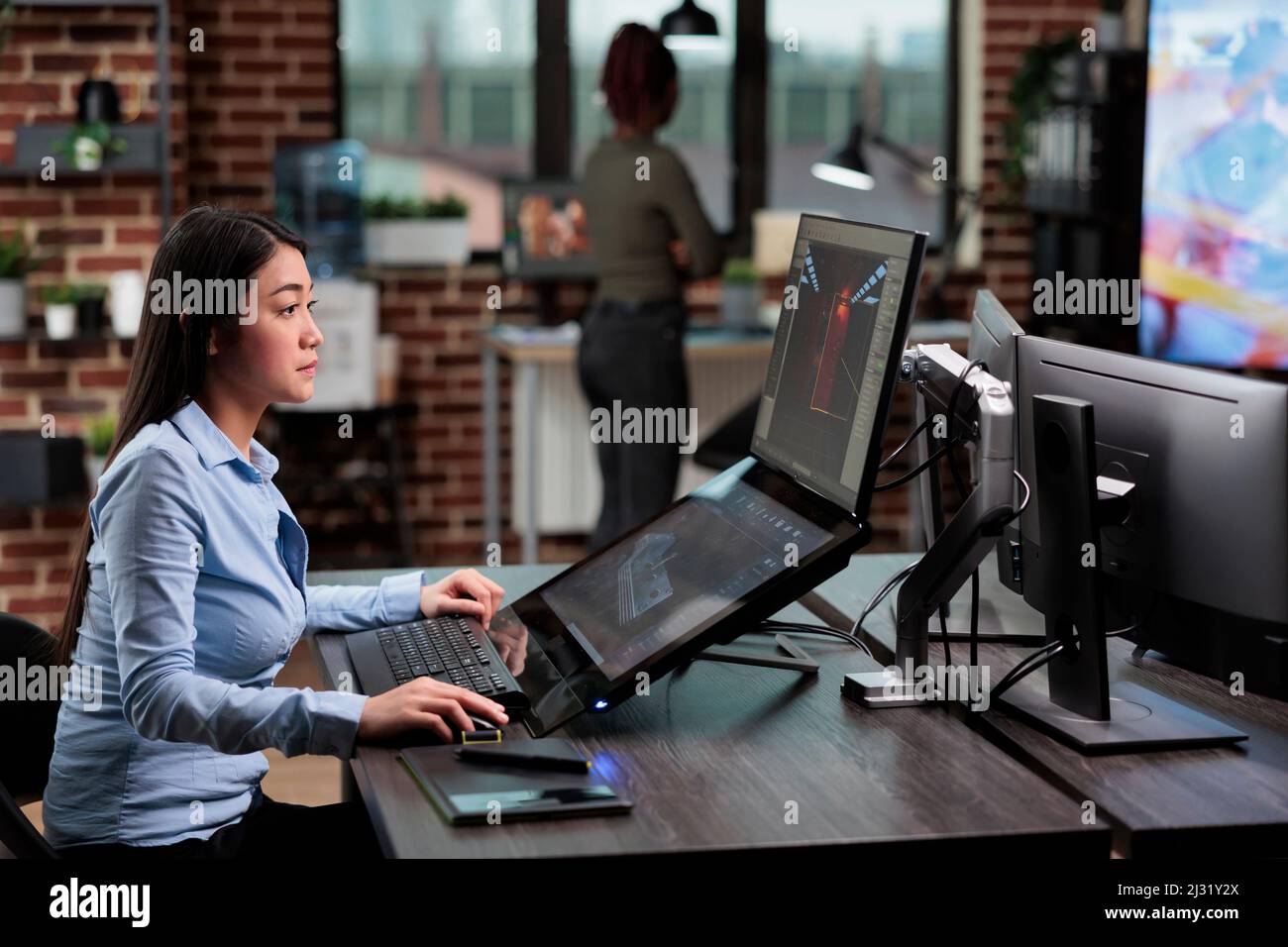 Creador del modelo asiático 3D sentado en el escritorio con varios  monitores mientras trabaja en CGI. Artista digital creando imágenes  generadas por ordenador para el desarrollo de juegos mientras se encuentra  en