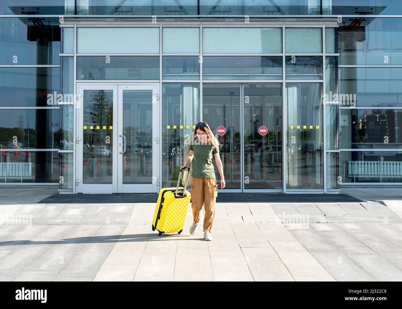 Mujer joven viajera con ropa informal llevando una maleta amarilla junto a la entrada del aeropuerto fuera del concepto de turismo de vuelos de viaje Foto de stock